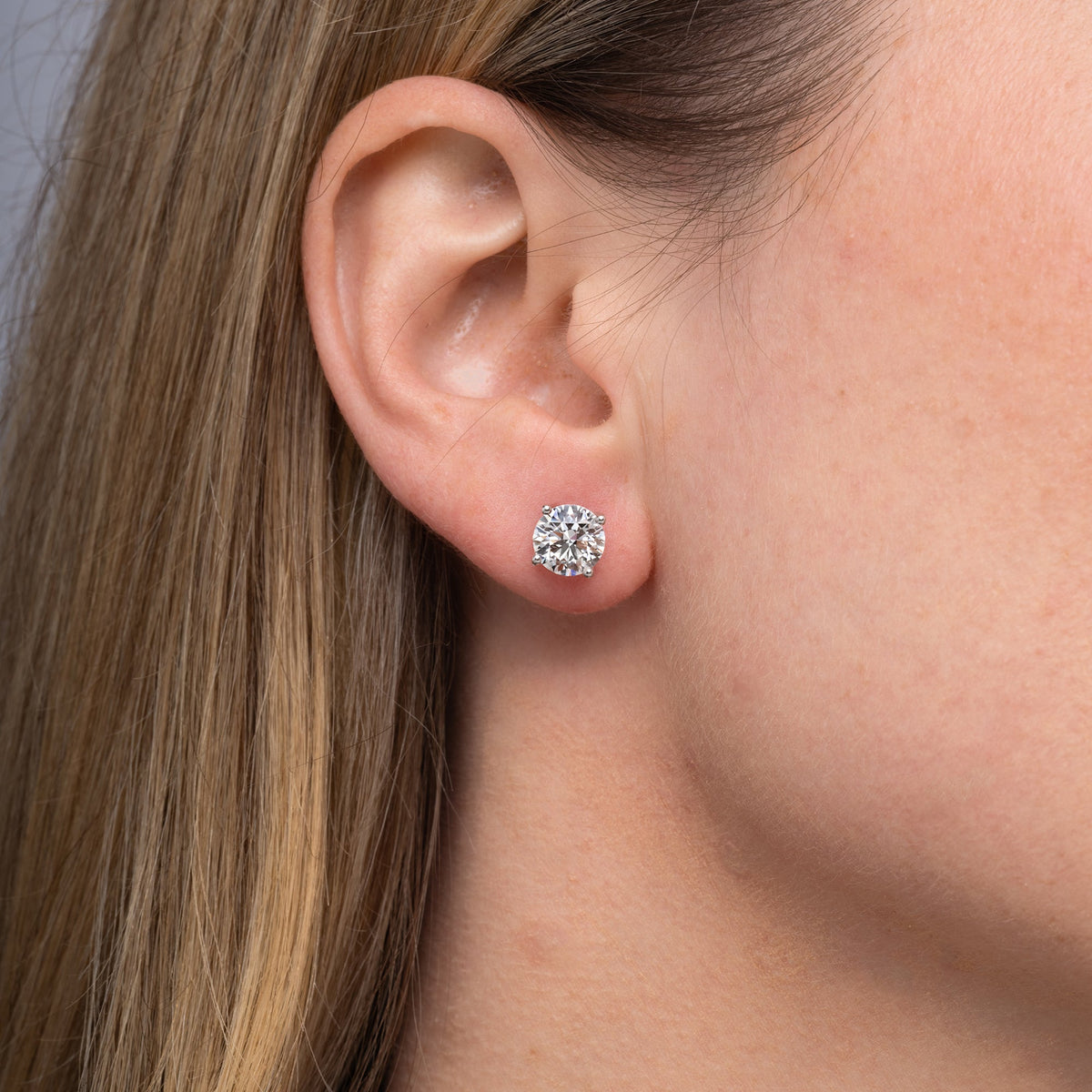 Round lab grown diamond stud earrings worn on the ear, 3.18 carat total weight