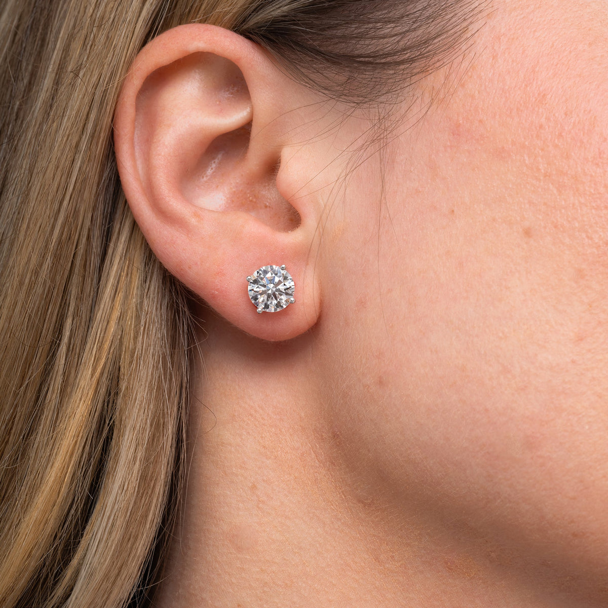 Round lab grown diamond stud earrings worn on the ear, 4.14 carat total weight