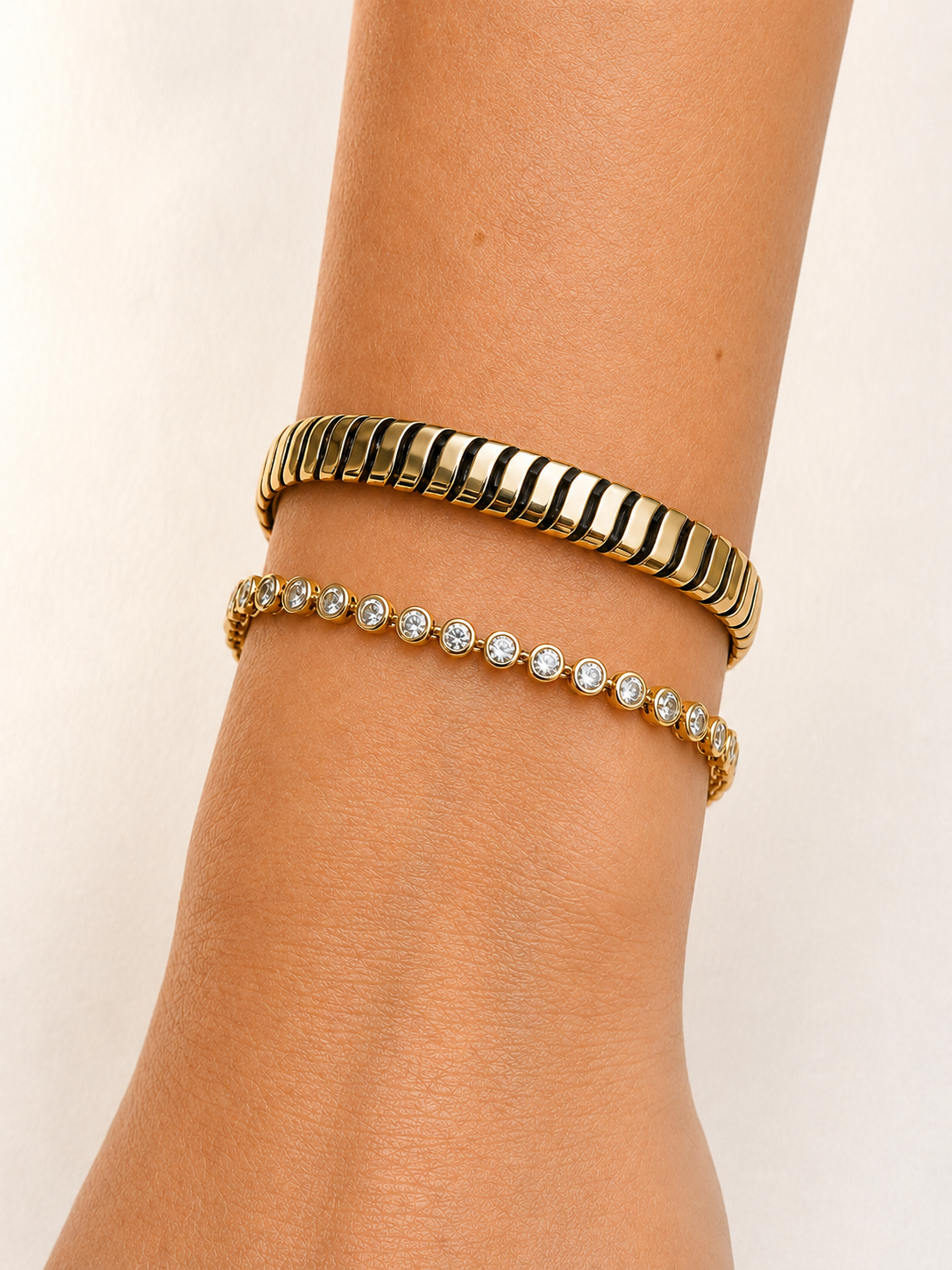 Bezel set diamond tennis bracelet in 14K yellow gold, worn on the wrist beside a wide gold cuff bracelet #Metal_Yellow Gold