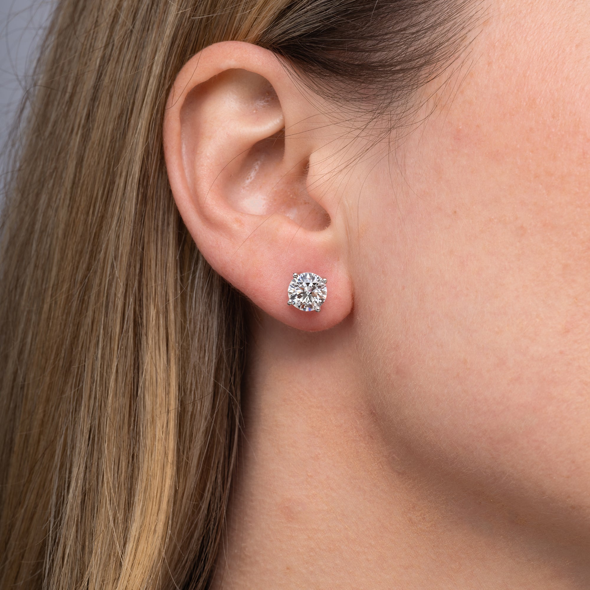 Round lab grown diamond stud earrings worn on the ear, 3.18 carat total weight