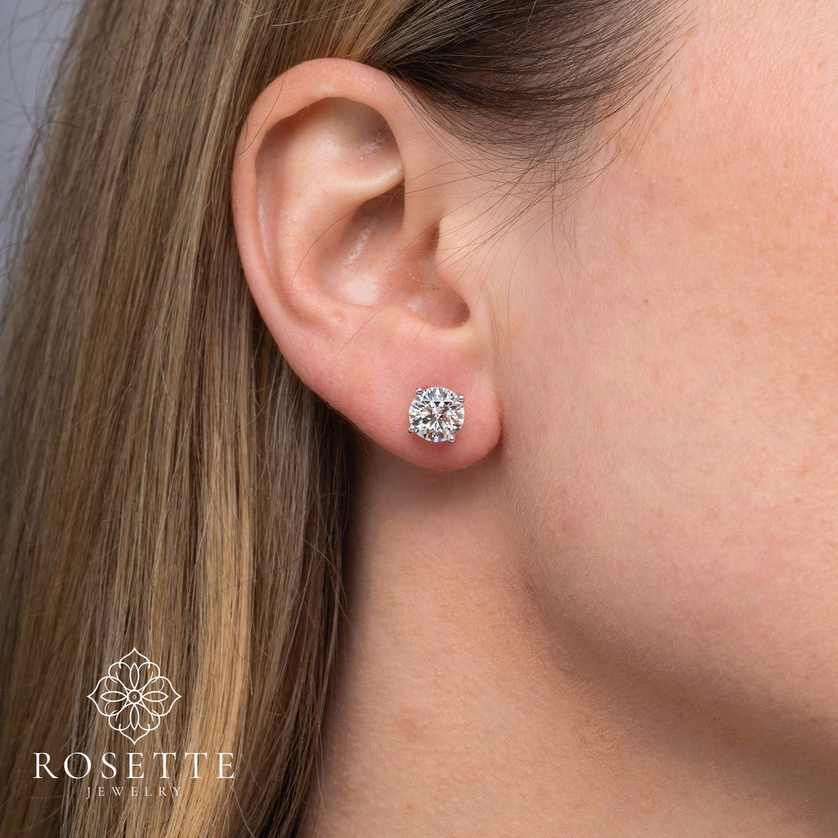 Round diamond stud earrings worn, showing scale on the earlobe